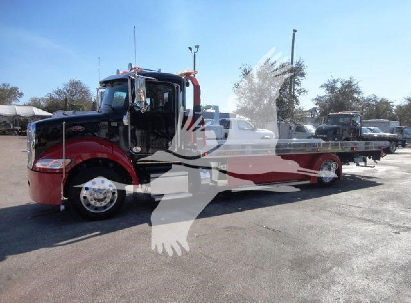 Peterbilt 337 rollback tow truck, side view, black cab with red fenders, long flatbed, chrome wheels, dealership lot in background.