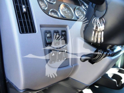 Truck interior of a 2022 Peterbilt 337 dashboard area showing ignition area with switches and gauges, steering column, keys hanging, and control panel near the left of the steering wheel.