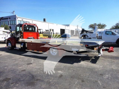 2022 Peterbilt 337 rollback truck in a dealership lot showing a long flatbed and red cab with chrome wheels.