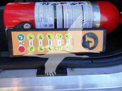 Truck equipment image showing a red fire extinguisher and a control panel with yellow circular icons mounted on a black surface inside a Peterbilt 337 rollback truck.