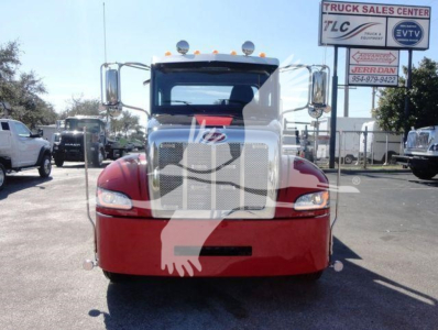 Peterbilt 337 rollback truck front view showing chrome grille, large bumper, and red lower body; signboards in background.