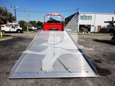 Aluminum rollback bed on a 2022 Peterbilt 337 chassis showing wide flatbed with tie-down anchors and front red cab in distance.
