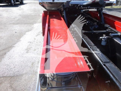 Peterbilt rollback truck chassis with red side rail and hydraulic components visible; partial view of hitch area and black frame, branding not legible.