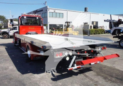 Peterbilt 337 rollback tow truck with flatbed, red cab, gray flatbed, rear lights, and towing equipment visible.
