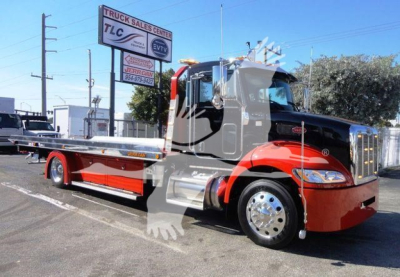 Peterbilt 337 rollback tow truck in red and black with flatbed, dealership sign in background, stock number J04652.