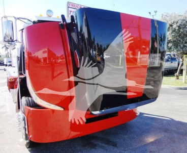 Peterbilt 337 rollback truck showing bold red and black paint scheme with cab tilted forward, windshield reflections, and side mirror.