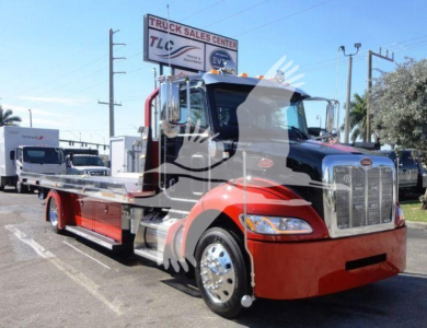 Peterbilt 337 rollback truck in front view with red cab and chrome grille, long wheelbase, loaders on a dealership lot.