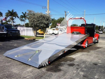 Peterbilt 337 rollback truck with a long folded aluminum ramp bed and red cab, showroom-style chrome accents, parked outdoors.