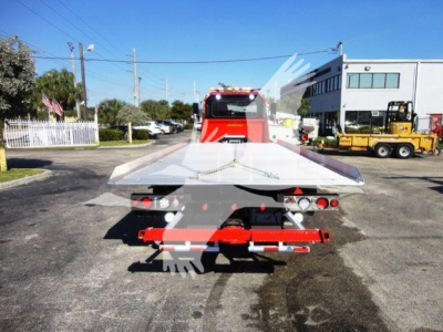 Peterbilt 337 rollback tow truck rear view with metal deck and red underride bumper, lights, and wheel chocks visible.