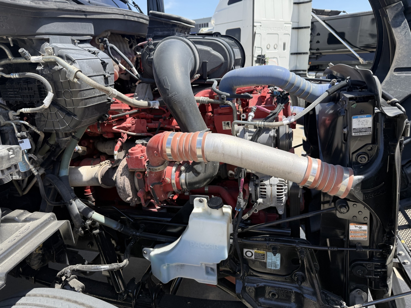 Peterbilt 579 engine bay with visible hoses, coolant reservoir, and air intake; red engine components and gray radiator area visible