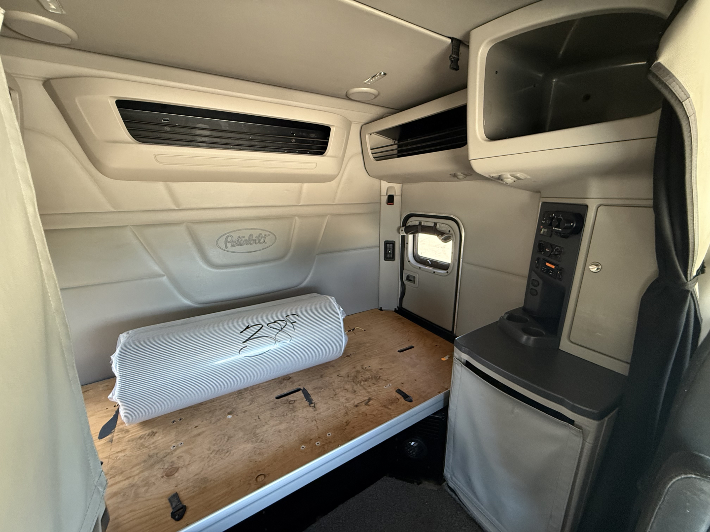 Peterbilt 579 truck cab interior sleeper area with storage area and dashboard panel visible, light gray interior and compact controls.