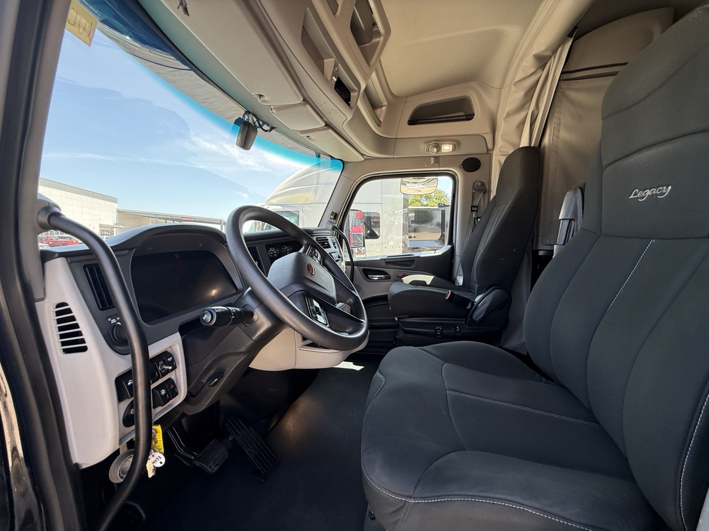 Peterbilt 579 truck interior showing steering wheel, driver seat, and dash with Legacy seating. Text on seats reads Legacy. Window and overhead console visible.