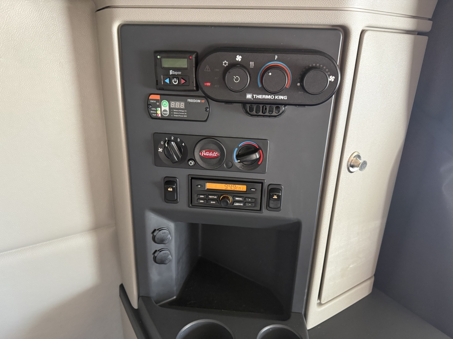 Panel inside 2023 Peterbilt 579 cab showing Thermo King HVAC controls, multiple switches, radio, and storage cubby.