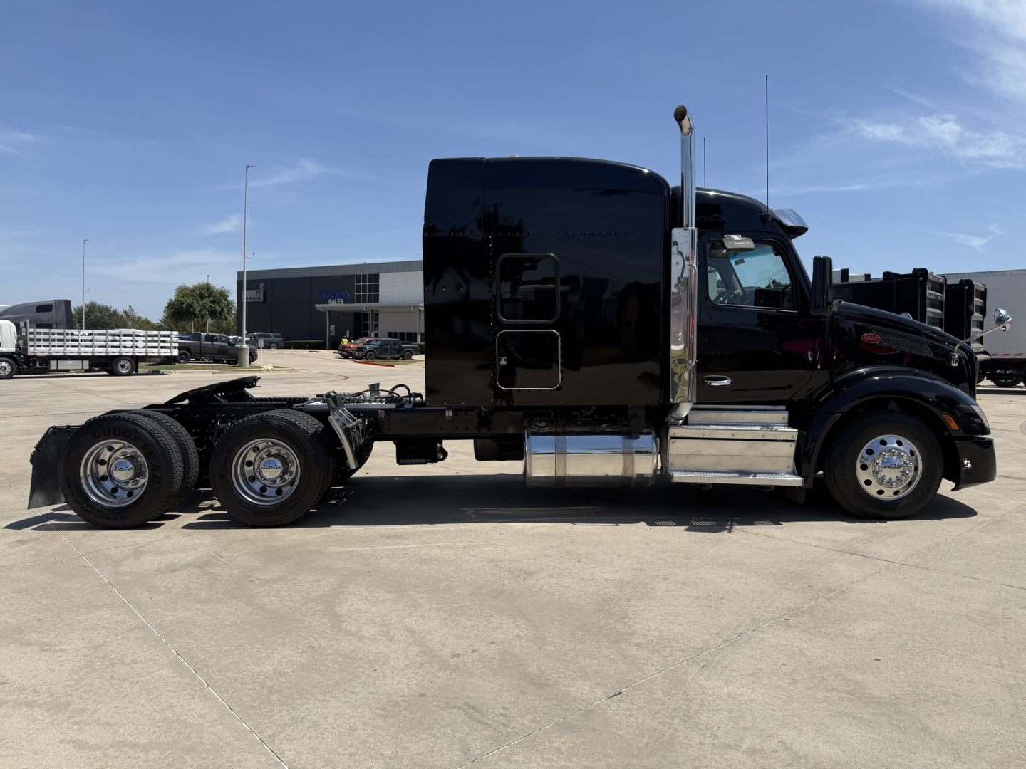 Peterbilt 579 with glossy black cab, sleeper, and multiple axles viewed in side profile showing exterior chrome fuel tanks and wheels.