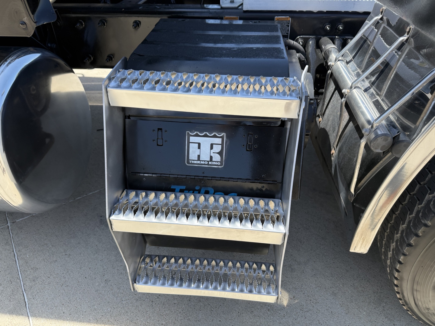 Step side of Peterbilt 579 showing aluminum diamond-plate step box and fuel/air tank area with steps and wheel well in view.