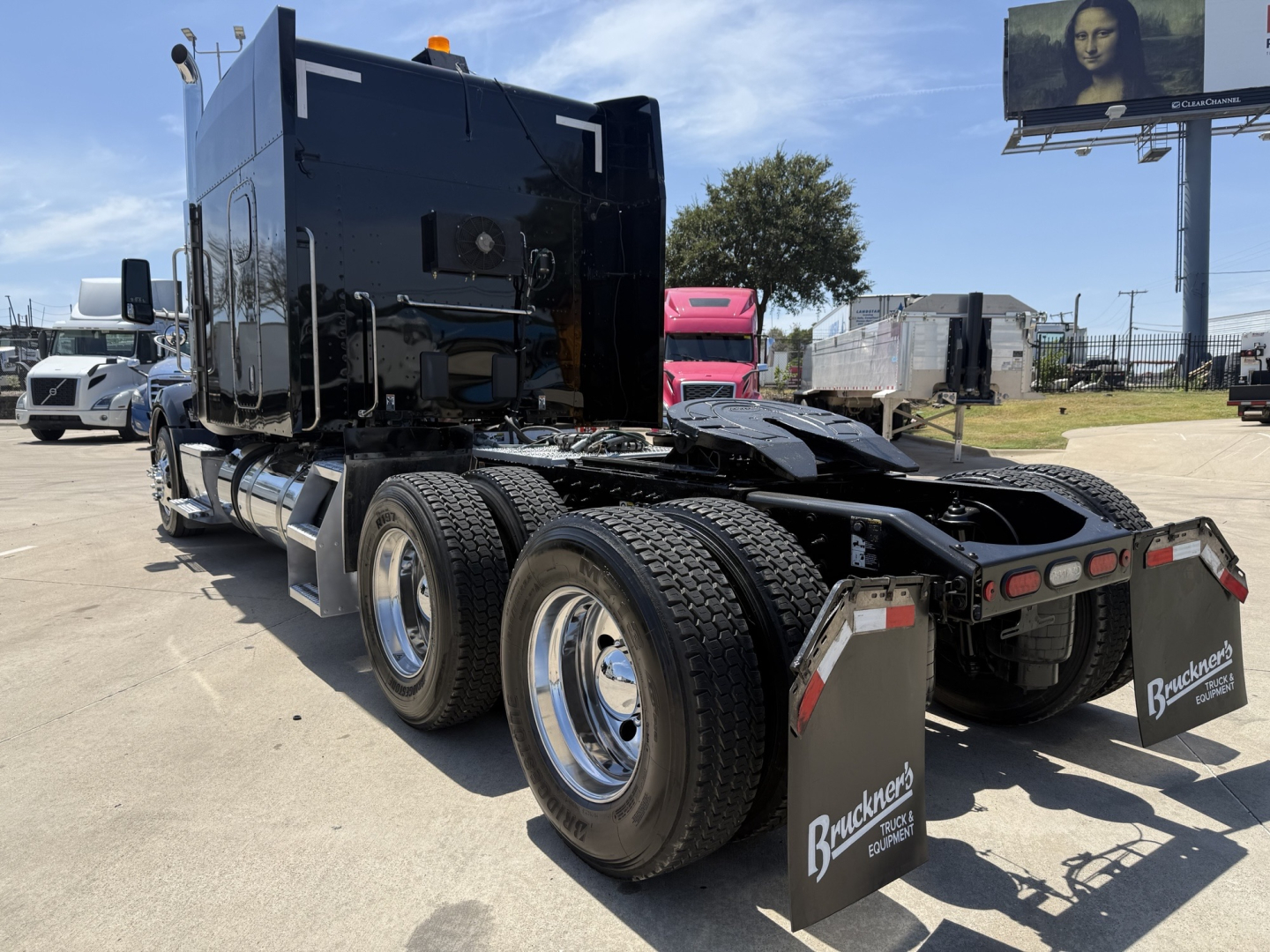 Peterbilt 579 tractor in a dealership lot, black sleeper cab, dual rear axles with chrome wheels, fifth wheel, mud flaps with Bracken’s logo, daytime clear sky