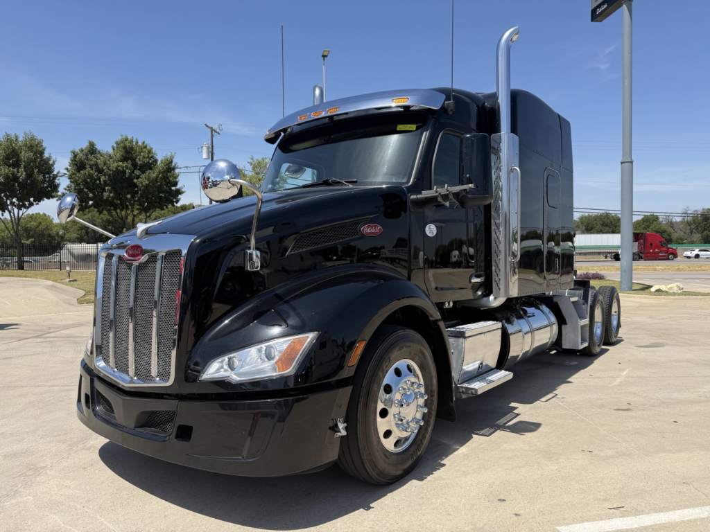 Peterbilt 579 conventional sleeper truck in black, front-left view, with chrome grille, dual exhaust stacks, large side fuel tanks, and chrome accents.