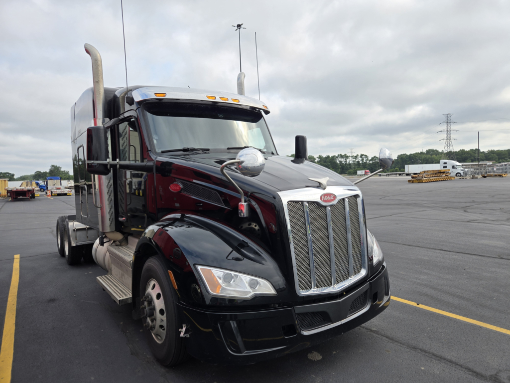 Peterbilt 579 truck in a parking lot, front angled view showing chrome grille, headlights, black paint, exhaust stacks, and side mirrors.