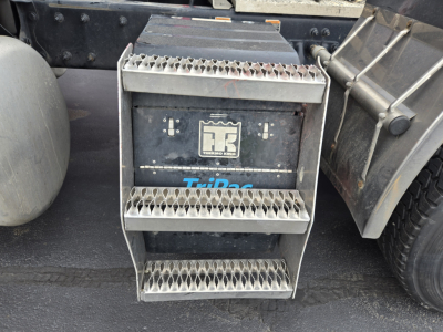 Peterbilt truck steps with TriPac auxiliary battery cabinet and TK logo on the side of the battery box. Visible text includes a recessed battery box with metal steps and a label reading 'TriPac' and a central emblem.
