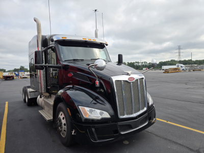 Peterbilt 579 truck in a parking lot, front angled view showing chrome grille, headlights, black paint, exhaust stacks, and side mirrors.