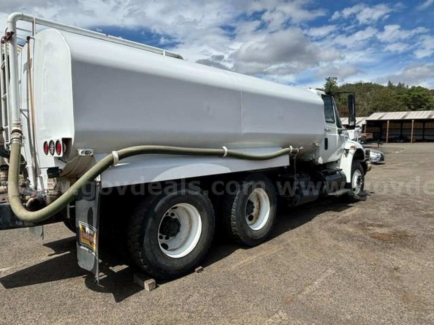 Truck-mounted tank with hose showing dual rear wheels and a large cylindrical tank; some text on the cab and tank obscured.