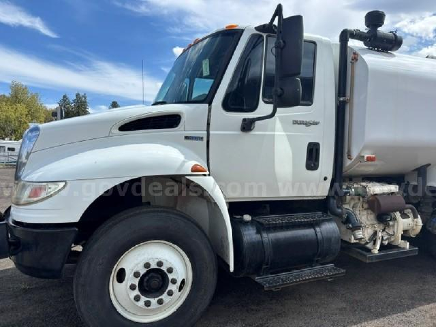 International 4400 truck with side-mounted fuel tank and water tank, front left view showing cab and wheel, model badge on door, and exhaust stack.