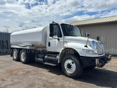 International 4400 dump truck in-service showing white tank body and dual rear axles with chrome grille and large side mirrors.