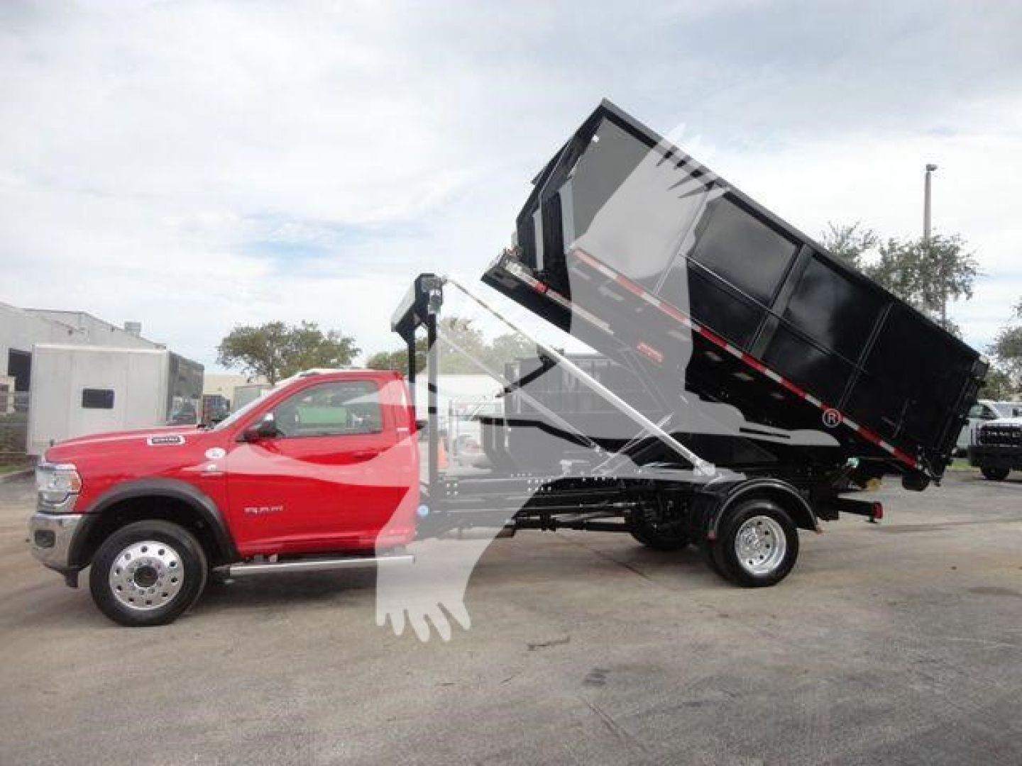 Ram 5500 dump truck with a raised black dump body on a red cab, hooklift truck in view