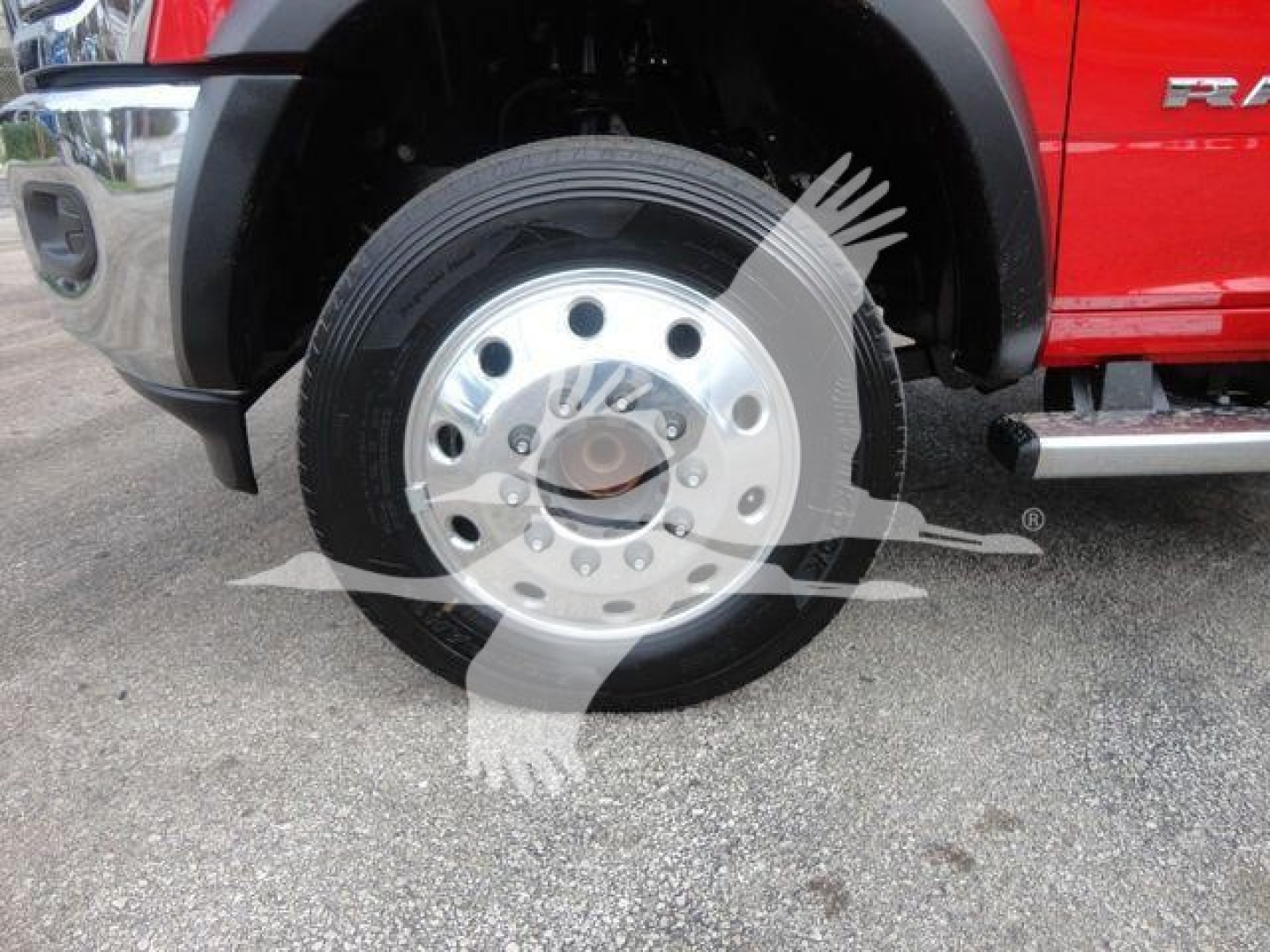 Ram 5500 front wheel: steel rim with multiple circular holes, tire mounted, red body side panel visible; part of heavy-duty truck with black fender and chrome step.