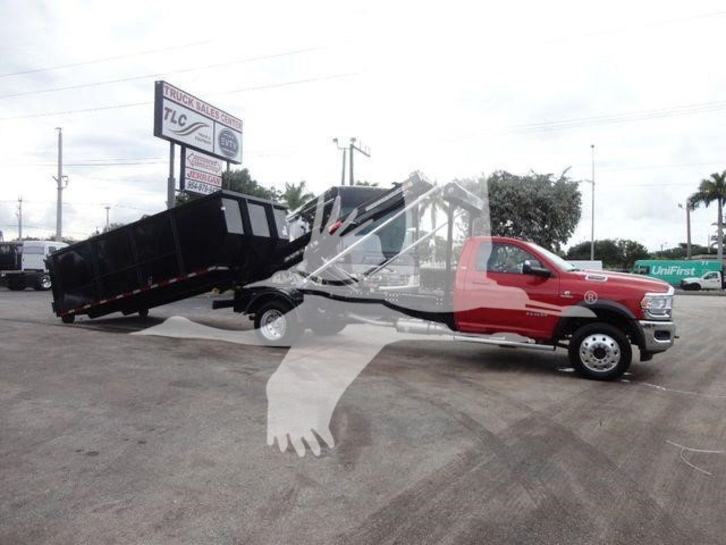 Ram 5500 dual-rear wheel truck with a hooklift bed in raised position, red cab and black dump bed in a dealership lot.