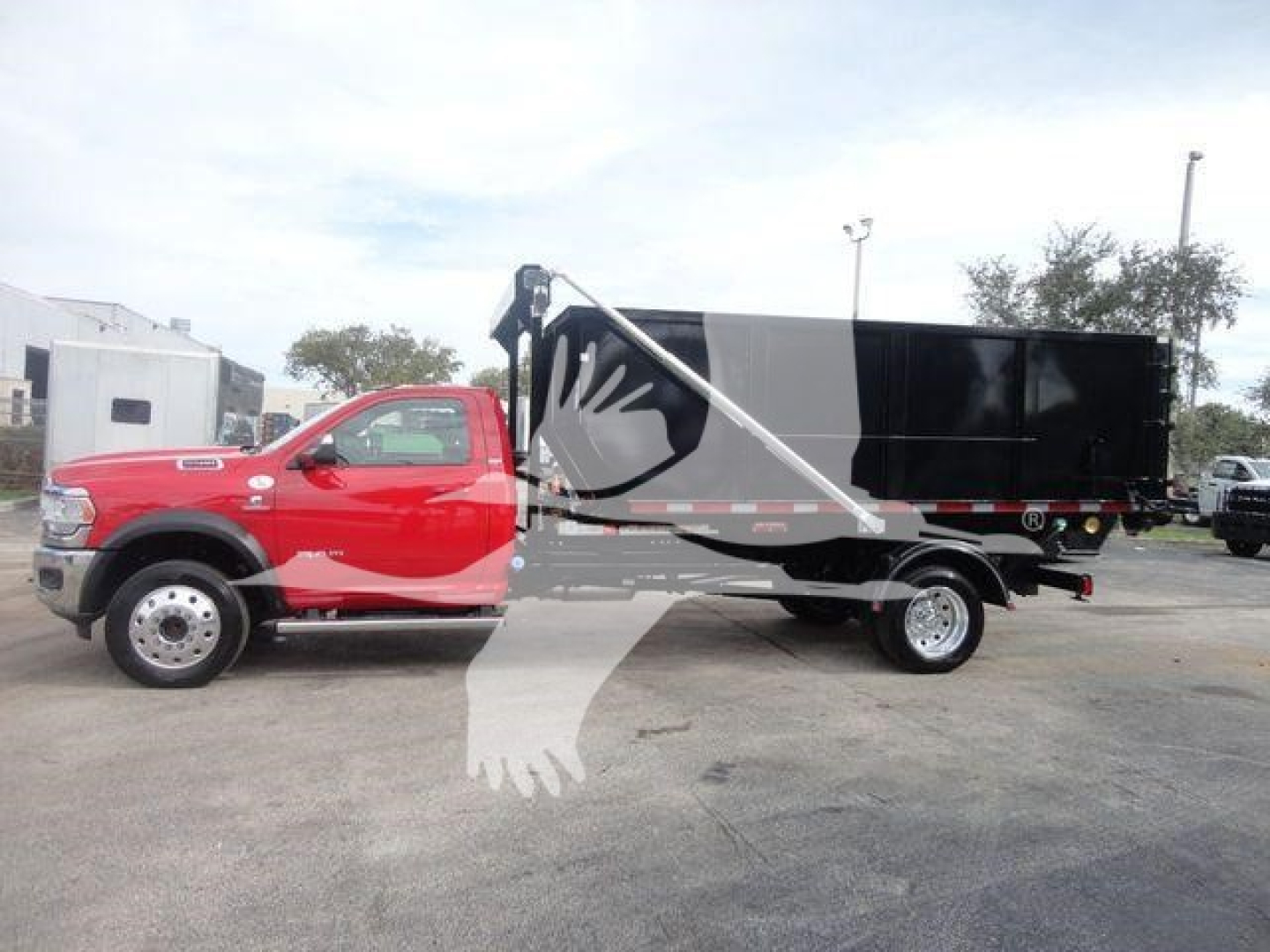 Truck side view showing a red Ram 5500 cab and a black hooklift cargo body with hydraulic lifting arm.