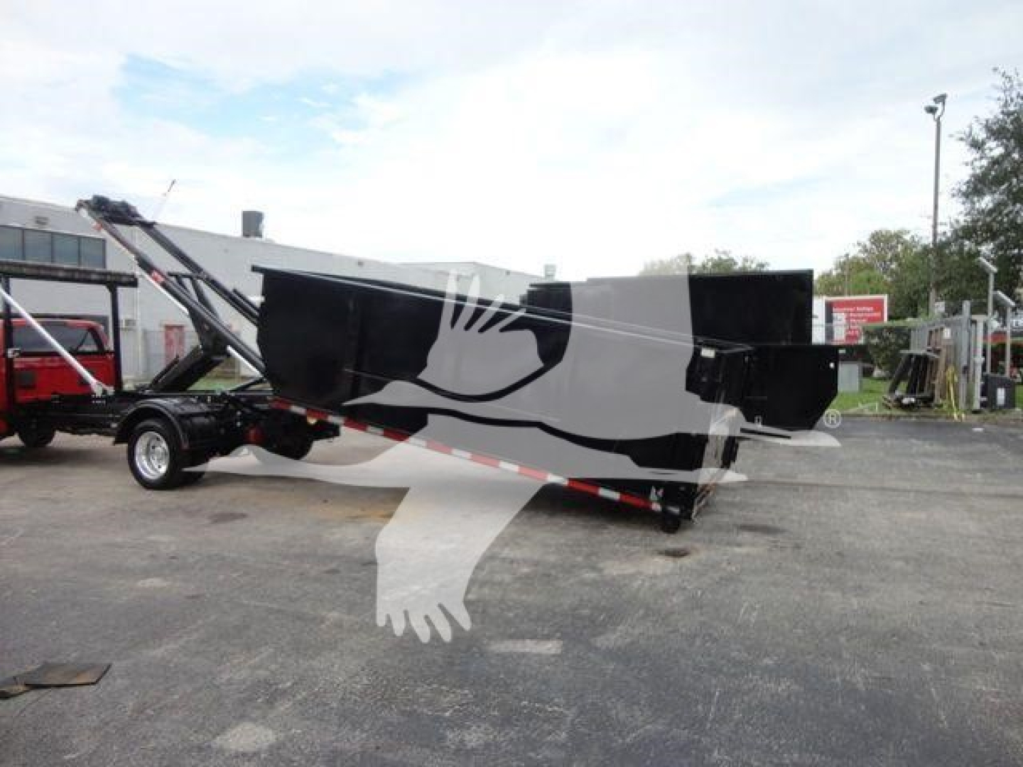 Flatbed truck with hooklift equipment showing a black dump body and trailing arms; no legible labels visible.