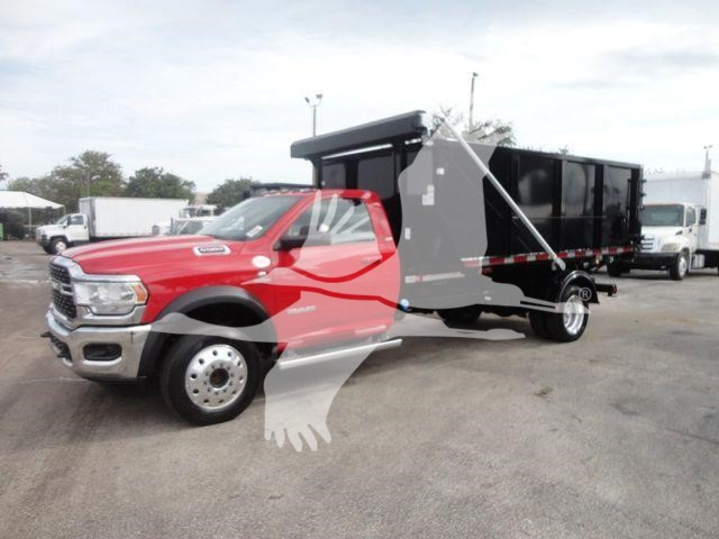 RAM 5500 cab with black dump/box body in a truck lot, red cab, hooklift configuration, side view showing front grille and dual rear wheels.