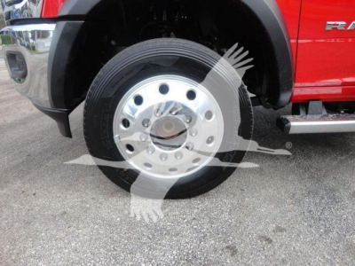 Ram 5500 front wheel: steel rim with multiple circular holes, tire mounted, red body side panel visible; part of heavy-duty truck with black fender and chrome step.