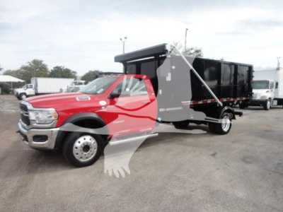 RAM 5500 cab with black dump/box body in a truck lot, red cab, hooklift configuration, side view showing front grille and dual rear wheels.