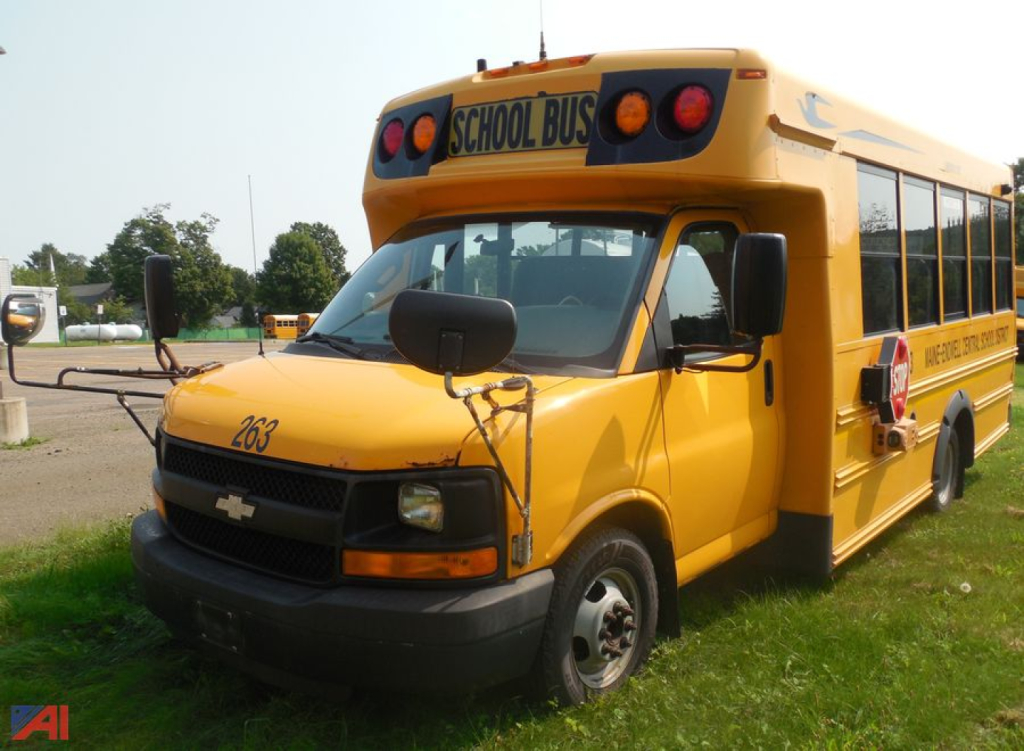 Chevrolet Express school bus in yellow with 'SCHOOL BUS' sign on top, front grille and side windows visible.