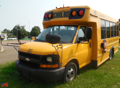 Chevrolet Express school bus in yellow with 'SCHOOL BUS' sign on top, front grille and side windows visible.
