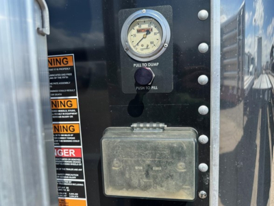 Hopper trailer control panel with a round gauge labeled 'PULL TO DUMP' and 'PUSH TO FILL', a weathered rectangular junction box beneath, and warning labels along the left edge.