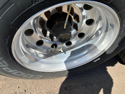 Wheel and tire close-up on a Timpte Super Hopper W trailer, polished steel rim with multiple circular holes, tire sidewall visible