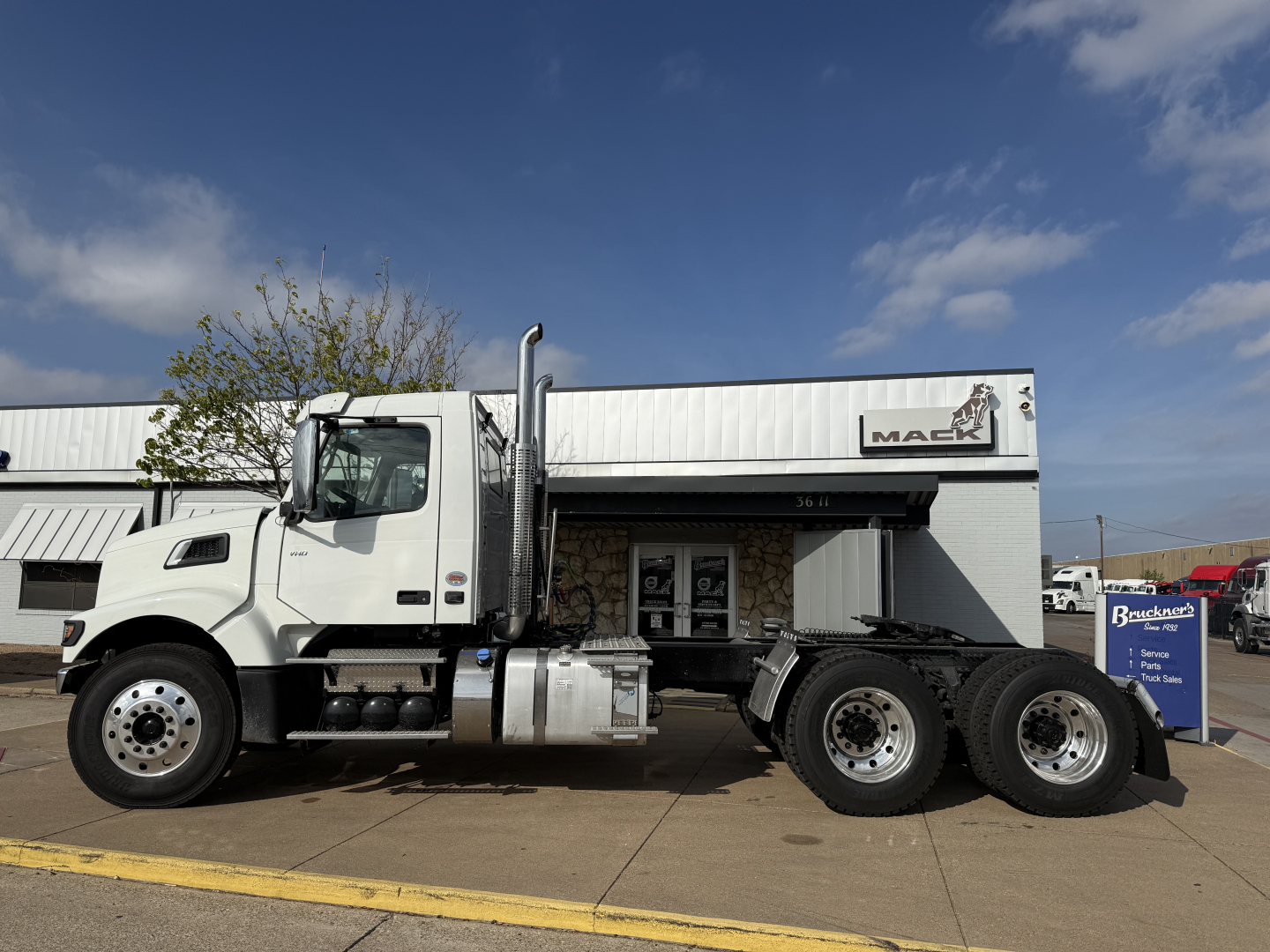 Volvo VHD64FT300 day cab truck in front of dealership, side view showing cab, fuel tanks, tandem rear axles and wheels.