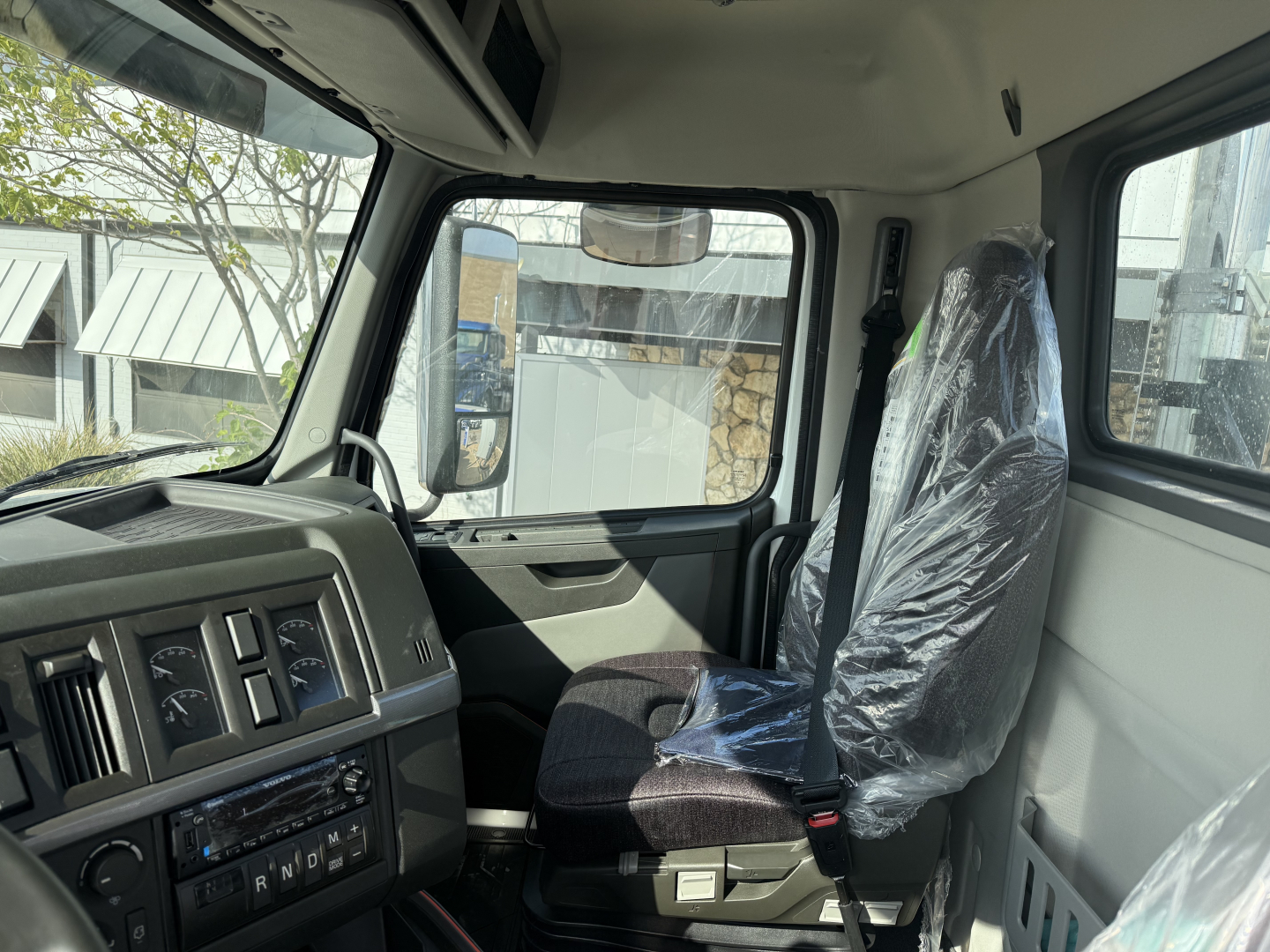 Interior cab view of a 2026 Volvo VHD64FT300 daycab showing driver seat with plastic cover, dashboard gauges, and door panels.