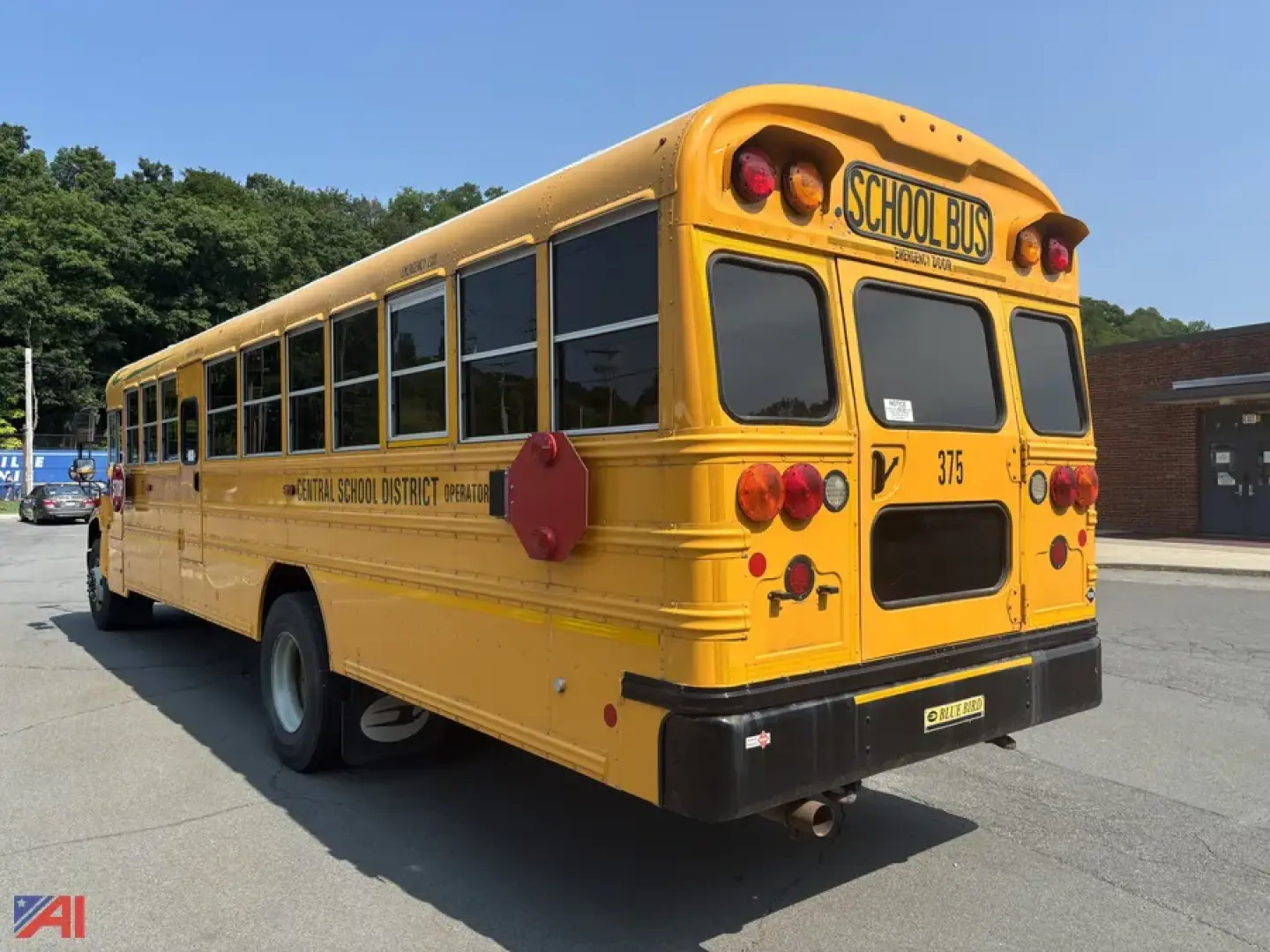 School bus rear/side view showing yellow BBCVB 3011 bus with rear lights, school bus sign, and 'Central School District' labeling on the side; blue sky and pavement background.