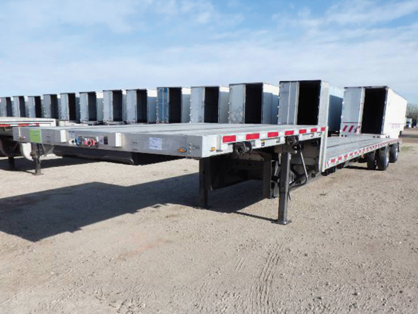 Trailer showing a Wilson aluminum and steel composite drop deck with open flatbed and side rails; visible VIN and stock numbers on the front area.