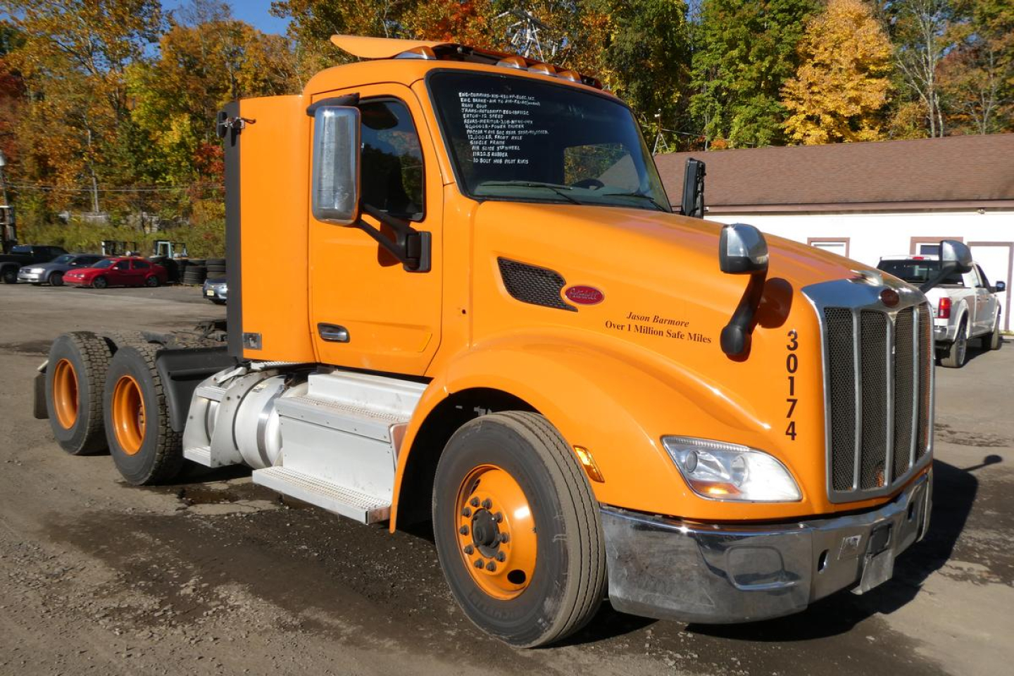 Peterbilt 579 truck in orange color, side view showing cab and front wheel, VIN sticker area on windshield, stock number 1015261.