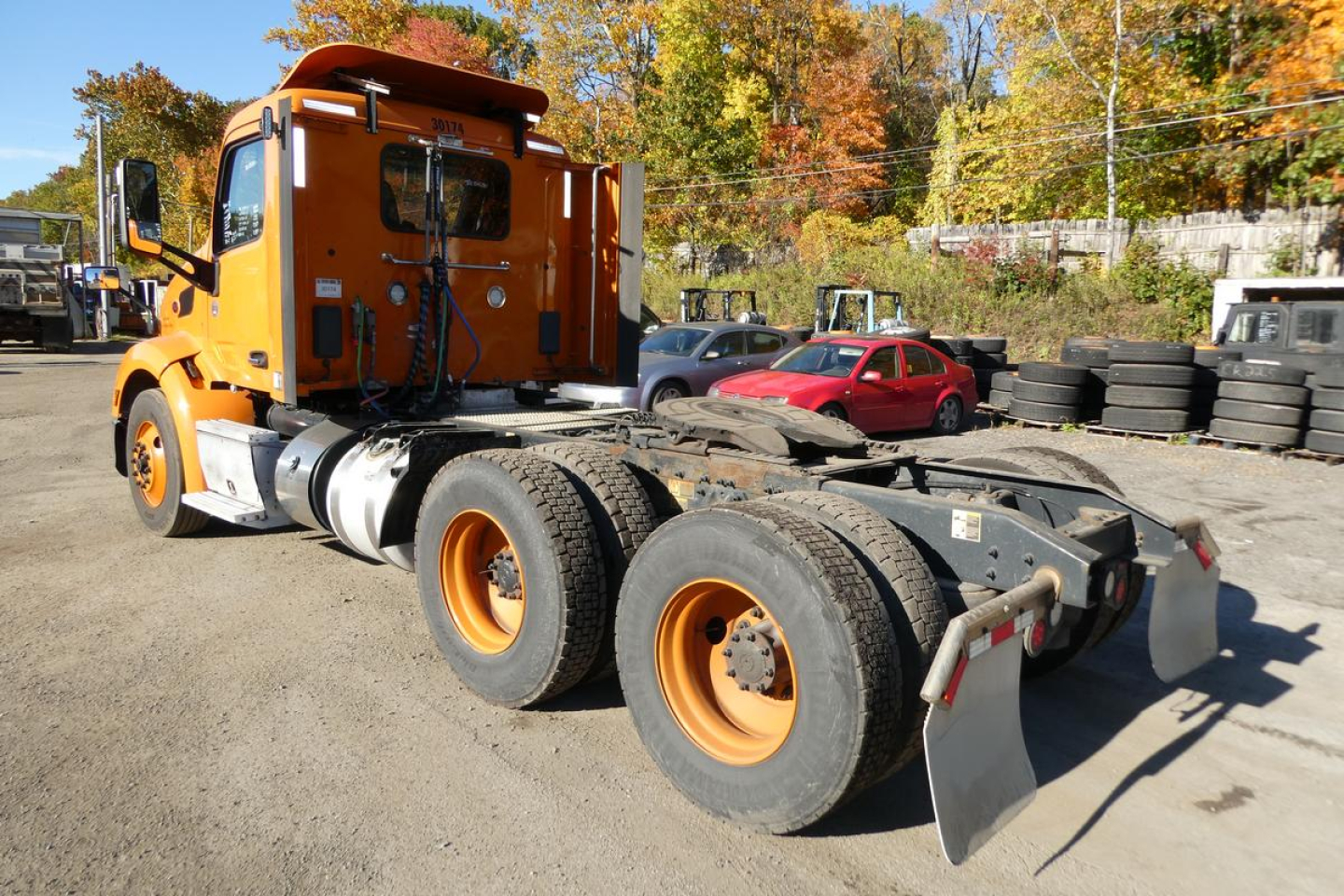 Peterbilt 579 road tractor in orange, cab view with triple rear axles and large wheels, viewed from the rear passenger side