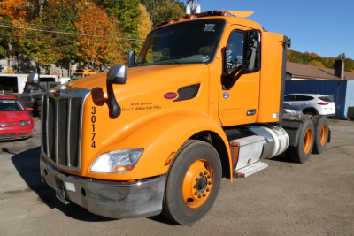 Peterbilt 579 tractor shows orange sleeper cab and front grille with large chrome bumper, dual rear axles, and fuel tanks; visible text on door area and driver-side window.