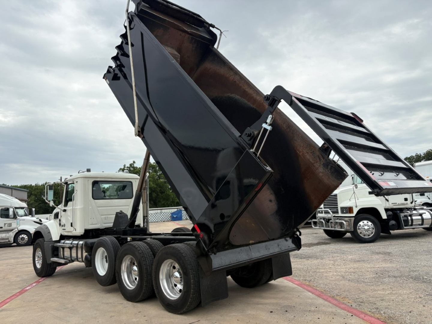 Dump truck in-service 2020 Mack GR64F with its dump bed raised, side view showing rear wheels and hydraulics.