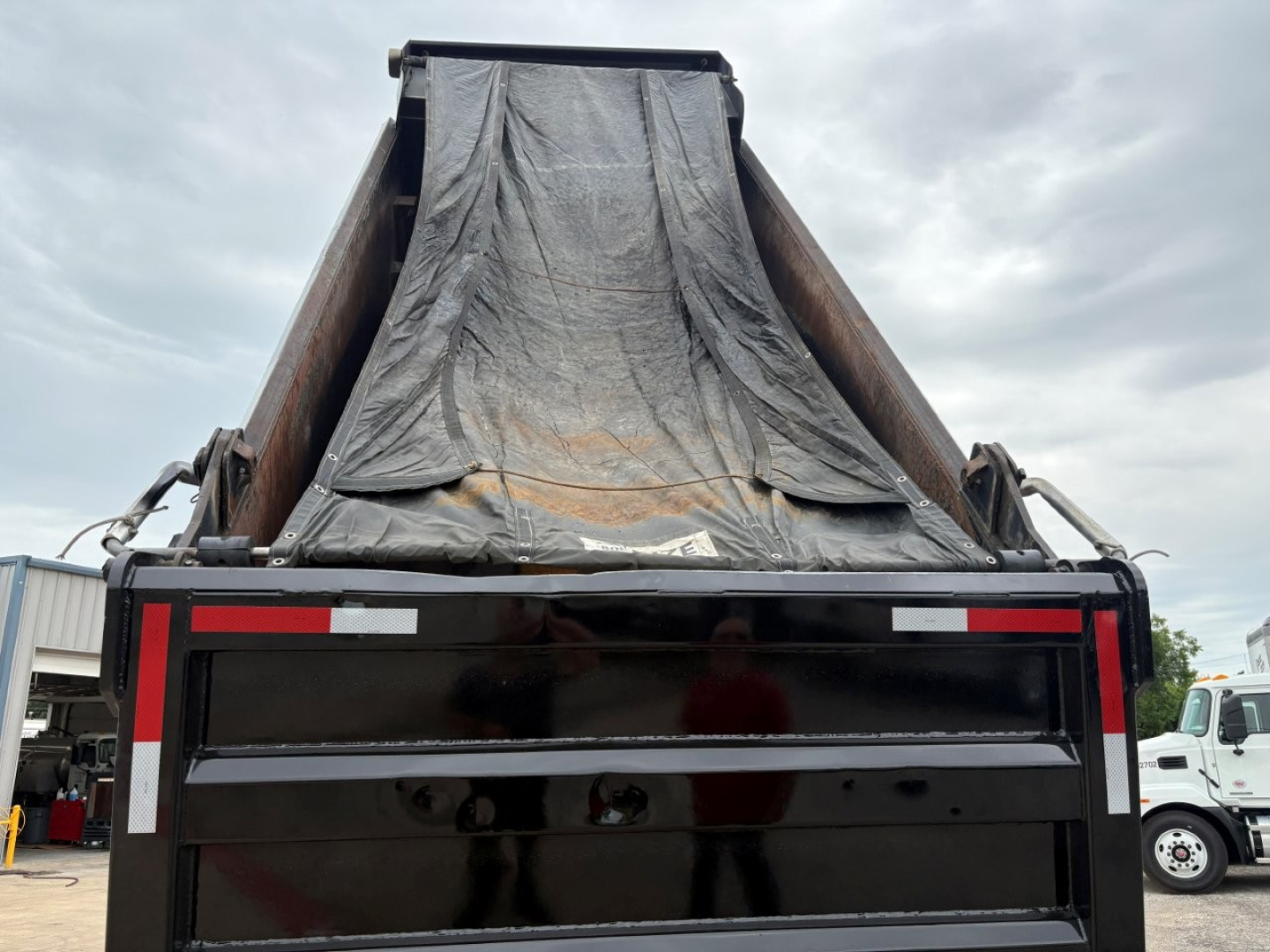 Dump truck bed of a 2020 Mack GR64F with tarp-covered dump box seen from rear, flat tailgate, black finish, and reflective safety markings.