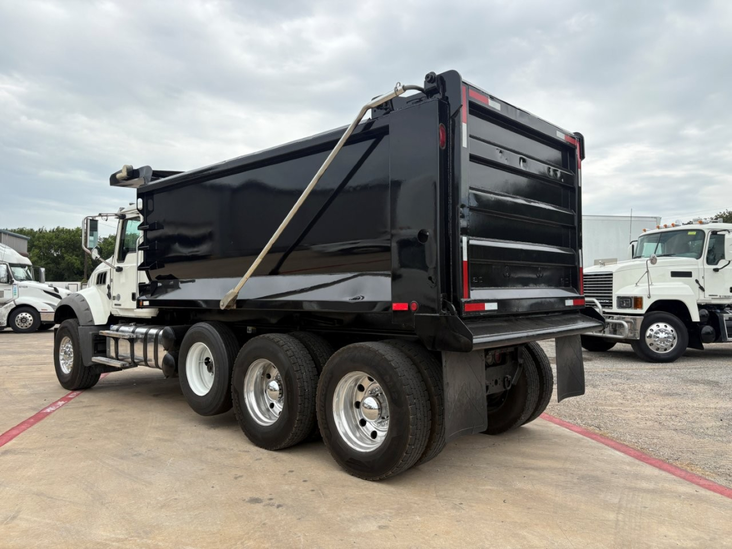 Dump truck rear-right view showing three axles and a black dump bed with side rails and hydraulic strap.