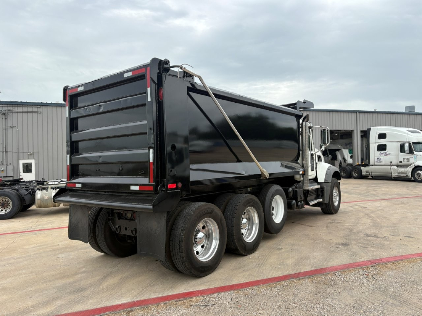 2020 Mack GR64F dump truck rear and side showing triple rear axles, black dump body, and chrome wheels.